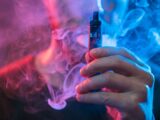 Hand haelt ein Vape-Geraet in dichter Dampfwolke mit blau-roter Beleuchtung, aufgenommen als Symbolaufnahme fuer intensiven Genuss mit Elfbar Liquids.